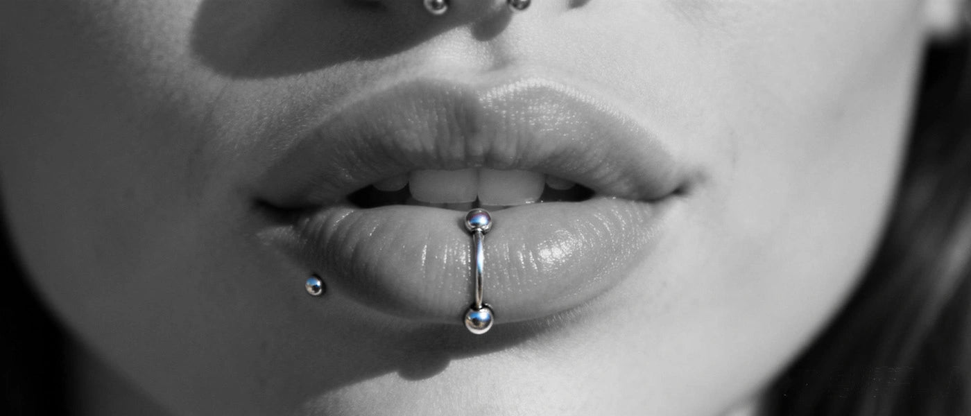 A stylized, intimate close-up that highlights the details of a silver lip ring piercing on a model's mouth.